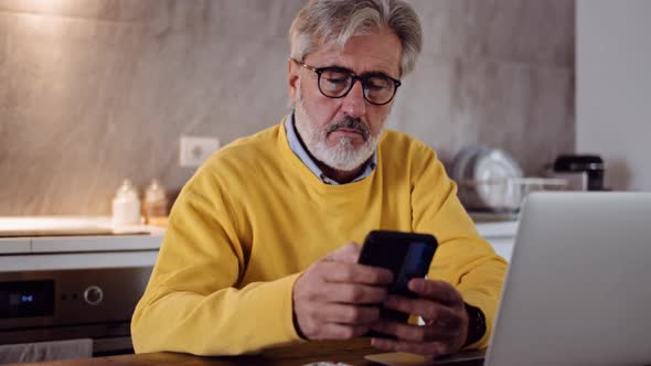 Slow motion shot of mature man using smartphone in the kitchen alt