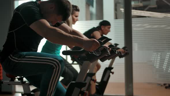 Athlete Adult Caucasian People Two Men and One Female Riding Bike Simulator alt