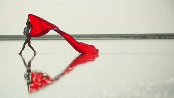 Woman Is Dancing in the Shallow Waters with a Big Red Piece of Fabric,  alt