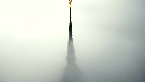 Drone Ascending Above Thick Fog To Reveal Majestic Golden Angel Statue alt