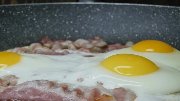 Chicken Eggs with Pork Bacon are Fried in a Frying Pan Closeup