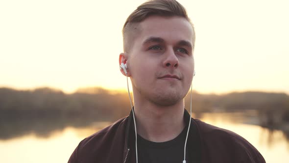 Young Handsome Cheerful Man Listens to Music on Beach During Sunset