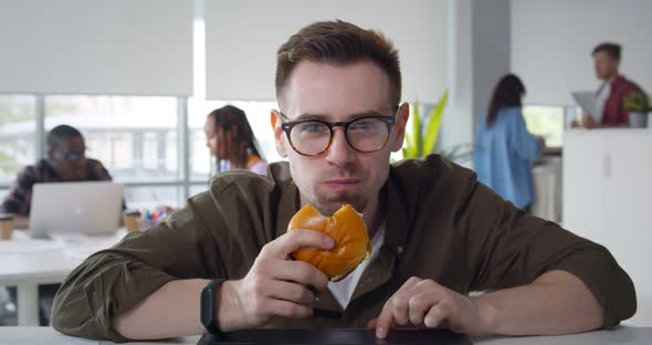 Man Having Lunch Break in Office Eating Takeaway Meal and Watching Video on Laptop alt