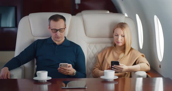 Mature Couple Drinking Coffee and Using Smartphone Flying on Private Jet alt