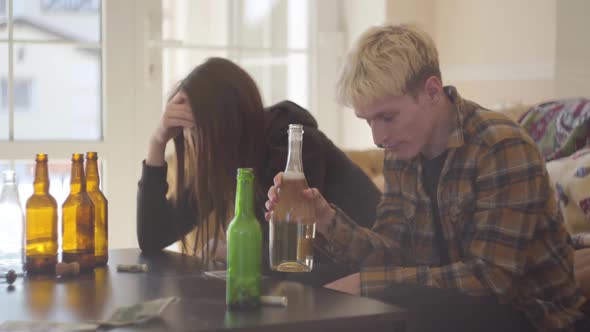 Young Woman and the Man with Colored Hair Sitting at Home in Front of Empty Alcohol Bottles alt