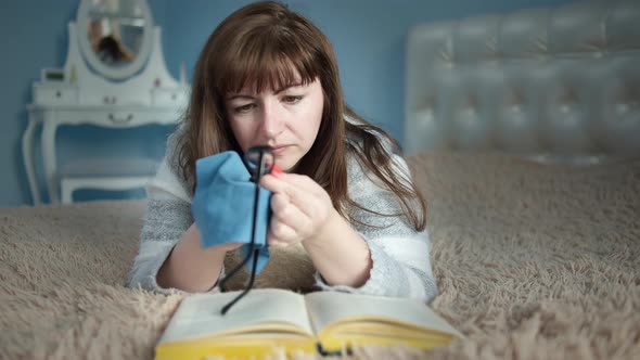 Woman Lies on the Bed and Wipes Her Glasses Before Reading a Book Day Off Reading a Book