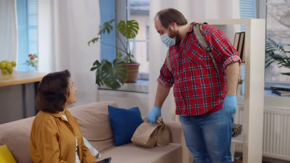 Man Courier on Protective Mask and Gloves Delivering Order To Senior Woman alt
