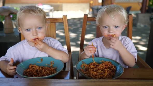 Two Caucasian Toddlers Develop Their Motor Skills By Eating Pasta with Hands alt