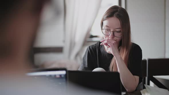 A young man and a young girl are working in front of laptops in their bright apartment. alt