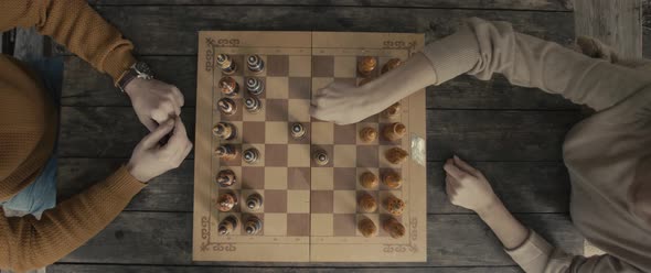 Adult people play chess sitting at wooden table at home