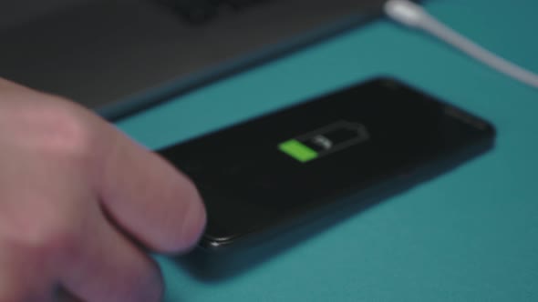 A hand inserts the usb-c cord into the smartphone and puts it next to the laptop to charge alt