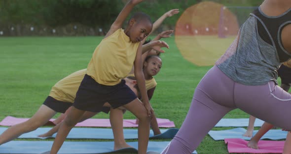 Mixed race female teacher showing diverse group of schoolchildren yoga stretching exercises outdoors alt
