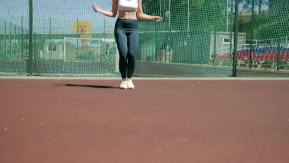 Young Woman in Sportswear Does Jump Exercise at Sports Ground with Skipping Rope