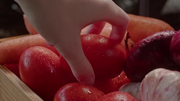 Woman's Hand Takes a Tomato From a Box of Vegetables