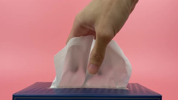 A person's hand pull out a piece of tissue from tissue paper box isolated on pink background.