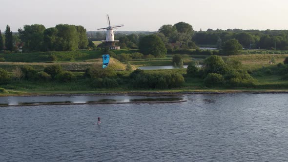 Beautiful Cinematic Aerial Drone Shot of Kitesurfing on a River Past an Old Windmill in Rural Nether alt