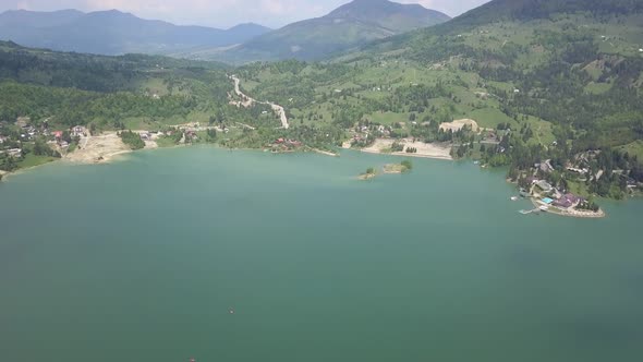 Aerial Downwards Panning shot of Lake with Green Forests on a sunny day alt