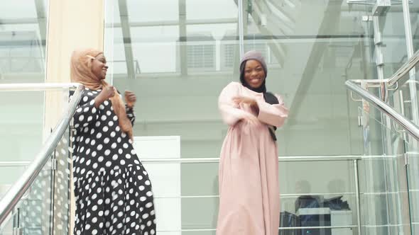 Two Positive Muslim Young Women Dancing on the Stairs in Modern Business Center
