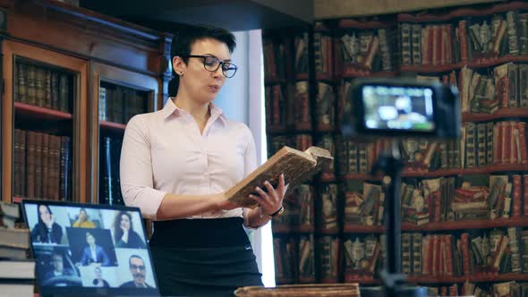 Female Teacher Is Talking About a Book During a Video Lesson alt