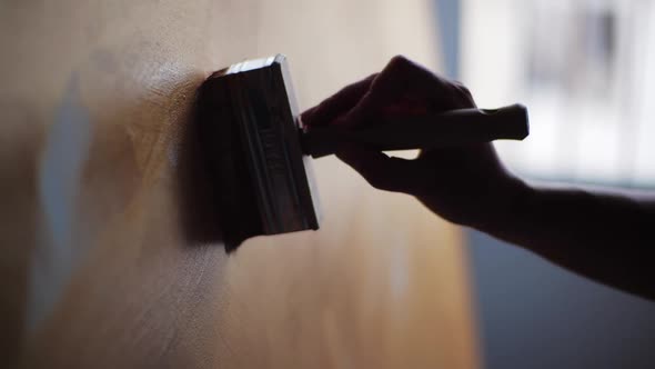 A Woman's Hand Draws a Graceful Line of Golden Brown Oil Paint with Brush on Light Canvas. Delicate alt