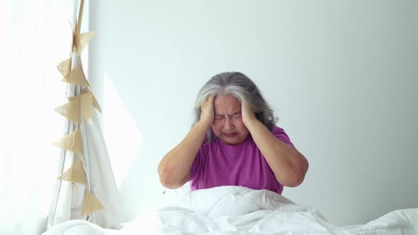 Senior woman with gray hair in bed feel depressed or suffering from strong headache migraine and hig alt
