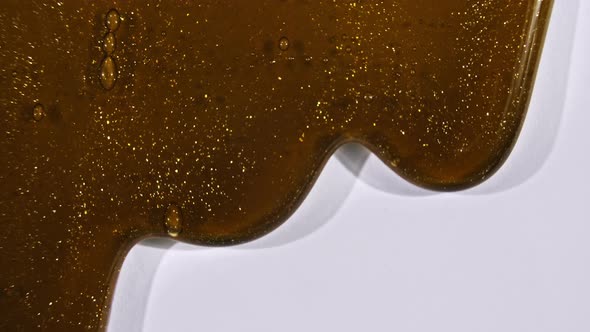 Brown Cosmetic Gel Fluid Gold Interspersed Flowing with Down on a White Surface alt