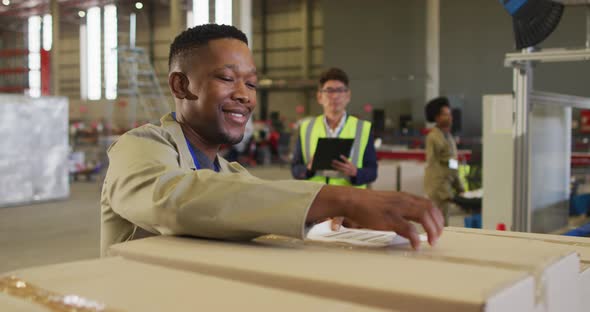 Diverse male workers with clipboard and boxes smiling in warehouse alt