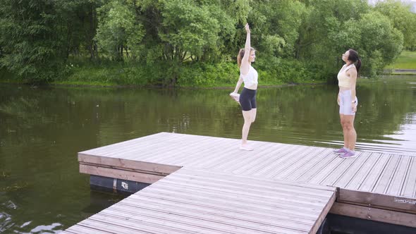 Girls Practice Exercises on Wooden Pier on Tranquil Pound