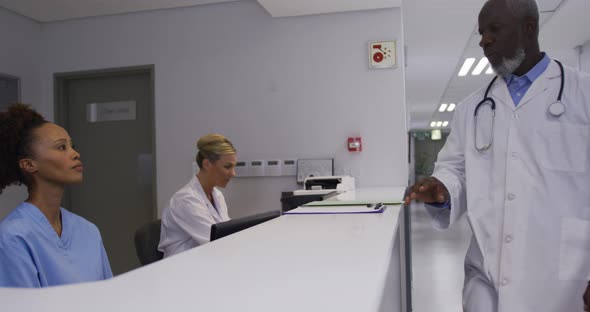 Diverse male doctor coming to hospital reception and talking to female staff alt