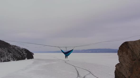 Man Sitting in a Hammock Mounted at High Altitude Over a Frozen Lake