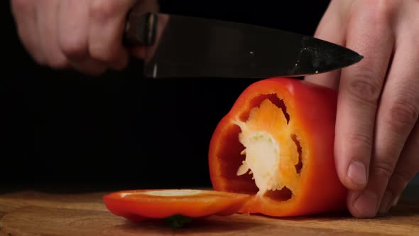 Knife cuts the red pepper in kitchen on wooden board. Close up. 4k