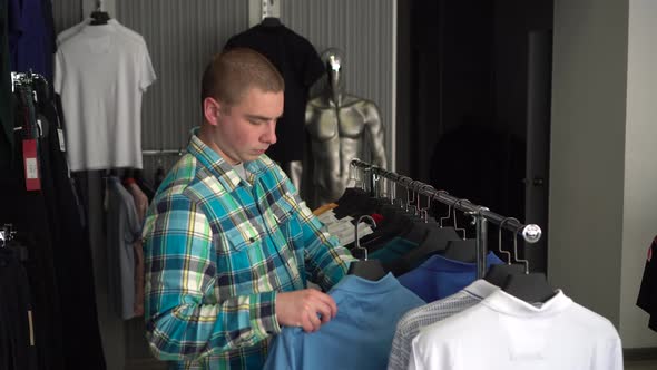 A Young Man Chooses a Shirt in a Store and Is Surprised at the Expensive Price of a Shirt. Clothing alt