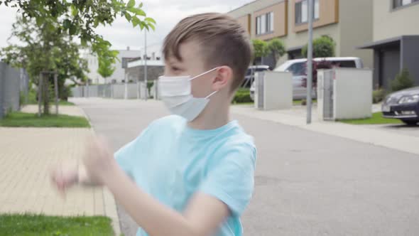A Young Boy Puts on a Face Mask and Dances in an Empty Suburban Area alt