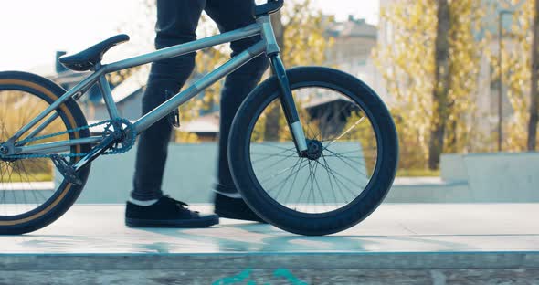 Teenager in Black Tight Pants Sneakers Walks Confidently Down Ramp at Skatepark Trees in Background alt