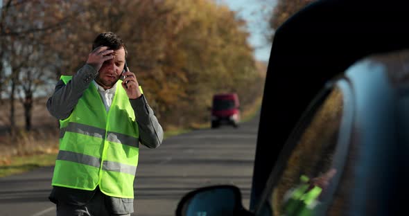 Portrait of Young Man in a Safety Vest Standing in Front of His Broken Car Looking at Car Engine and alt