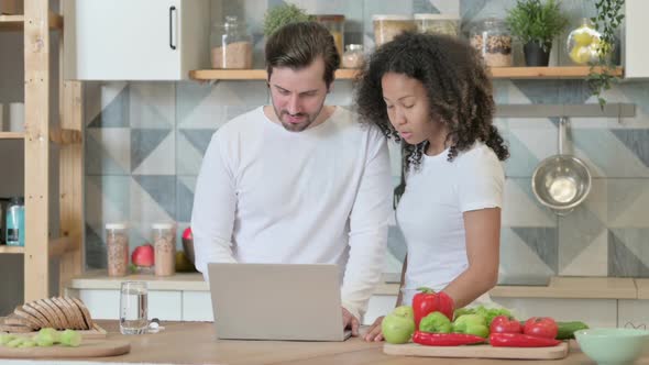 Mixed Race Couple Working on Laptop in Kitchen alt