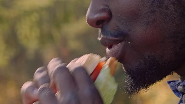 man biting off and chewing burger on the street