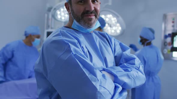 Portrait of caucasian male surgeon standing in operating theatre smiling to camera alt