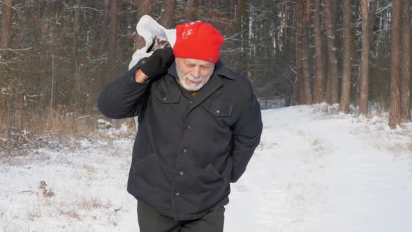 Aged Man Walks Along Snowy Road Holding Axe and Bag alt