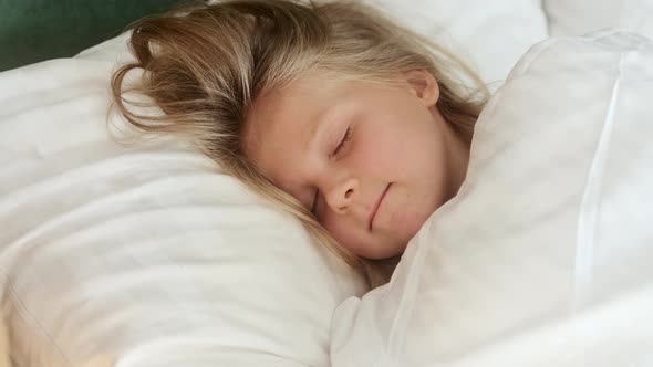 Little kid girl sleeping well in bed on pillow white linen orthopedic mattress. alt