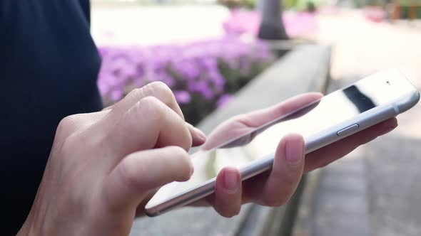 sian young woman sitting at bench in park using smartphone for talking, reading and texting.