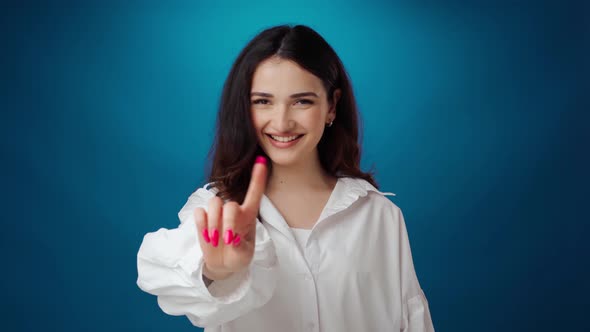 Smiling Young Woman Showing 'Stop' Gesture Against Blue Background