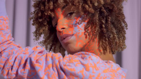 Mixed Race Woman with Curly Hair and Bright Neon Makeup Pattern on the Face the Same Like on Her