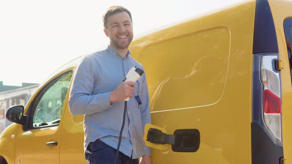 A Happy Man with a Charger at a Charging Station alt