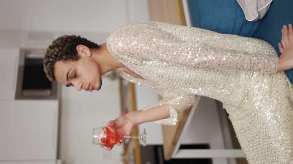 A Smiling Man in a White Dress Sitting on a Bed and Drinking Wine alt