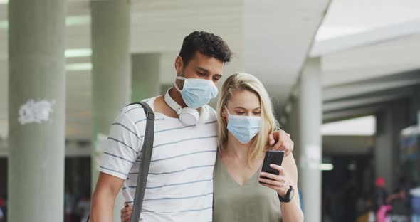 Caucasian couple on the go wearing a coronavirus covid19 mask and using phone alt