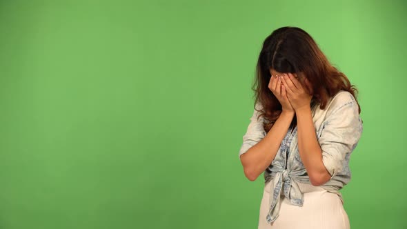 A Young Beautiful Caucasian Woman Cries with Her Hands Over His Face  Green Screen Background