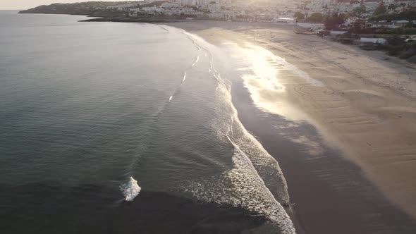 Calm waves roll on shimmering Praia da Luz Shoreline, Algarve. Aerial alt