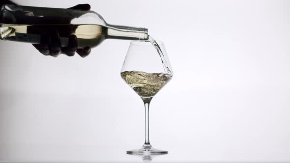 Pouring White Wine From a Clear Glass Into an Glass on a White Background alt