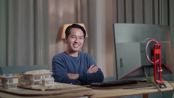 Engineer With House Model Smiling And Crossing His Arms To The Camera While Working On A Desktop alt